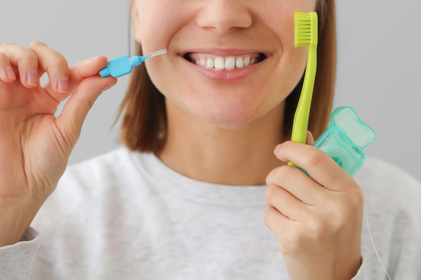A smiling woman cleaning between her teeth with an interdental brush